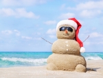 Smiling sandy snowman in red santa hat on the sea beach.